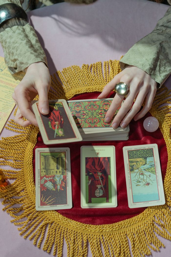 A mystical scene of a fortune tellers hands arranging tarot cards on a fringed cloth.