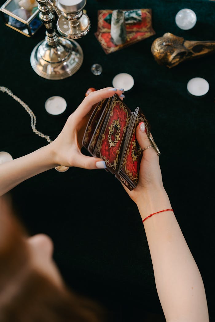 From above of crop unrecognizable female soothsayer shuffling tarot cards while reading future during esoteric session