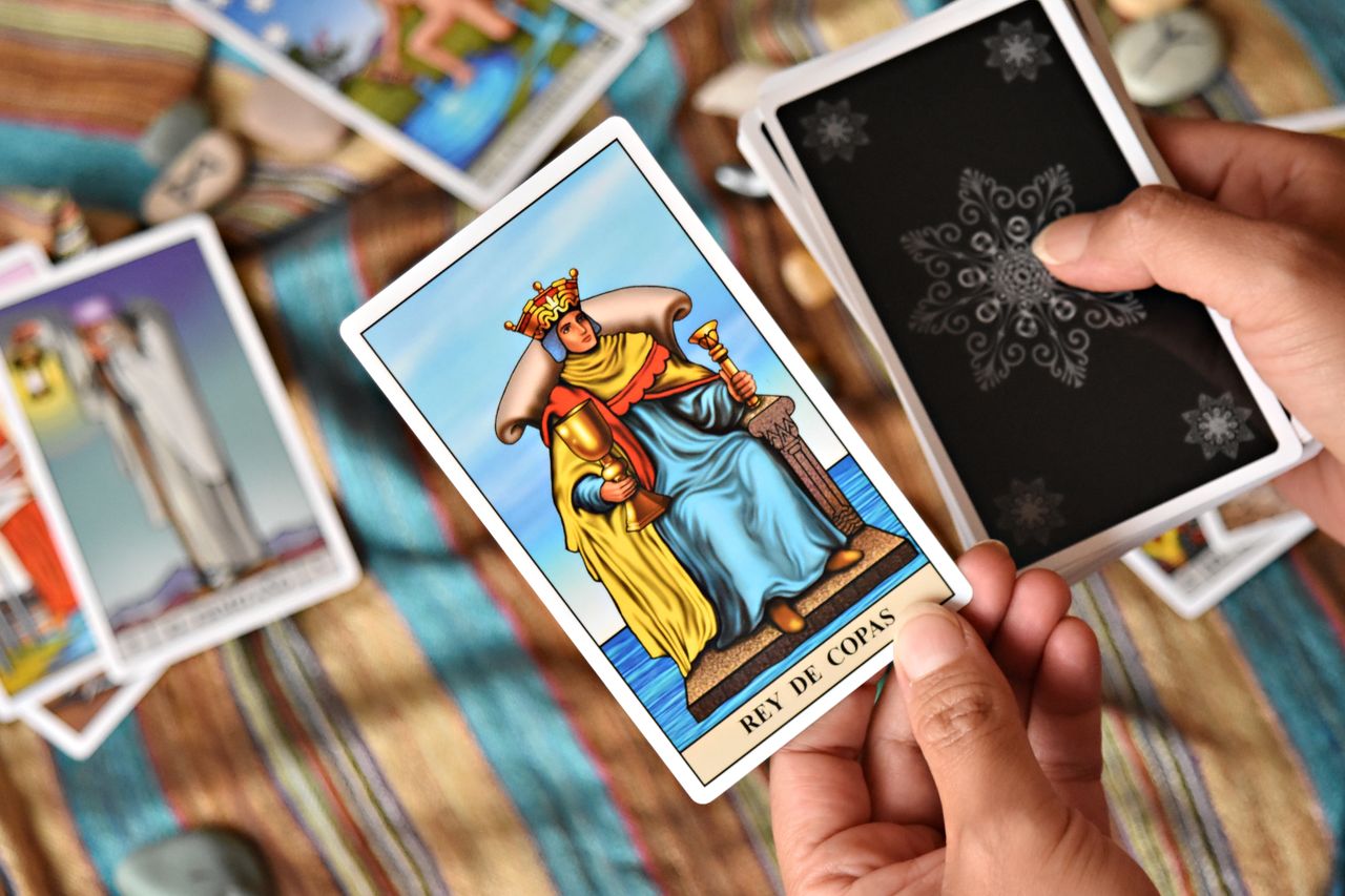 Closeup of hands holding tarot card Rey de Copas on colorful fabric.
